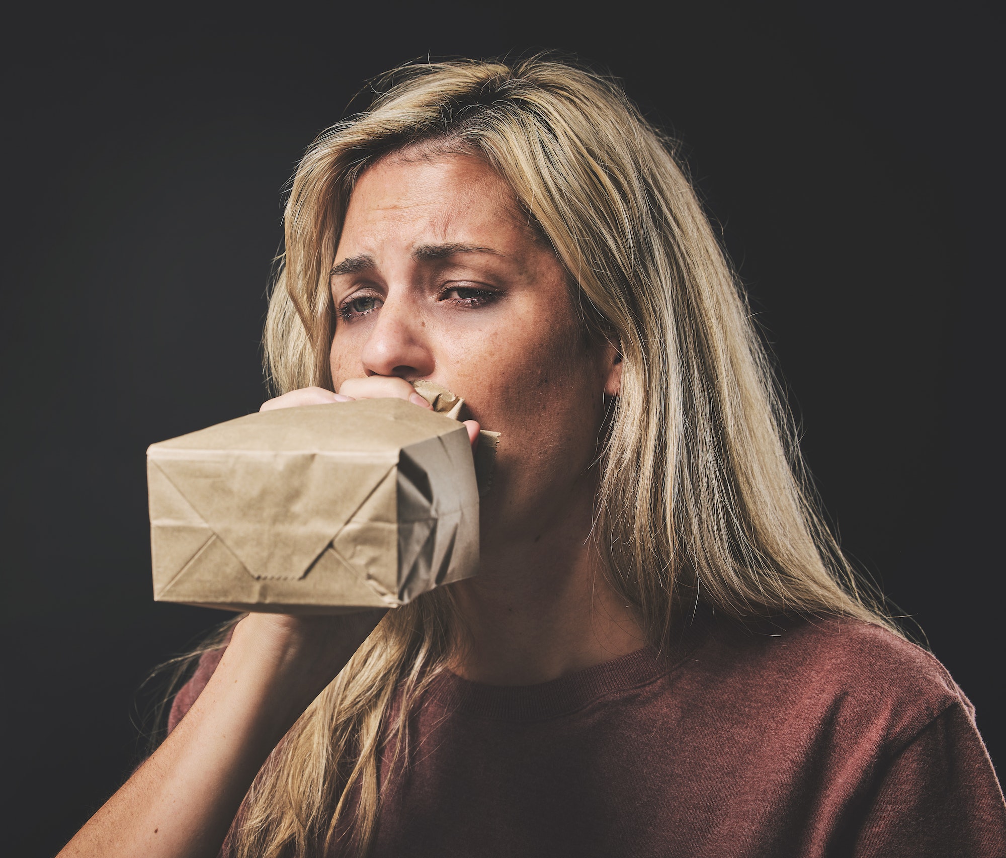 Anxiety, scared woman breathing into paper bag on dark background for mental health or psychology m