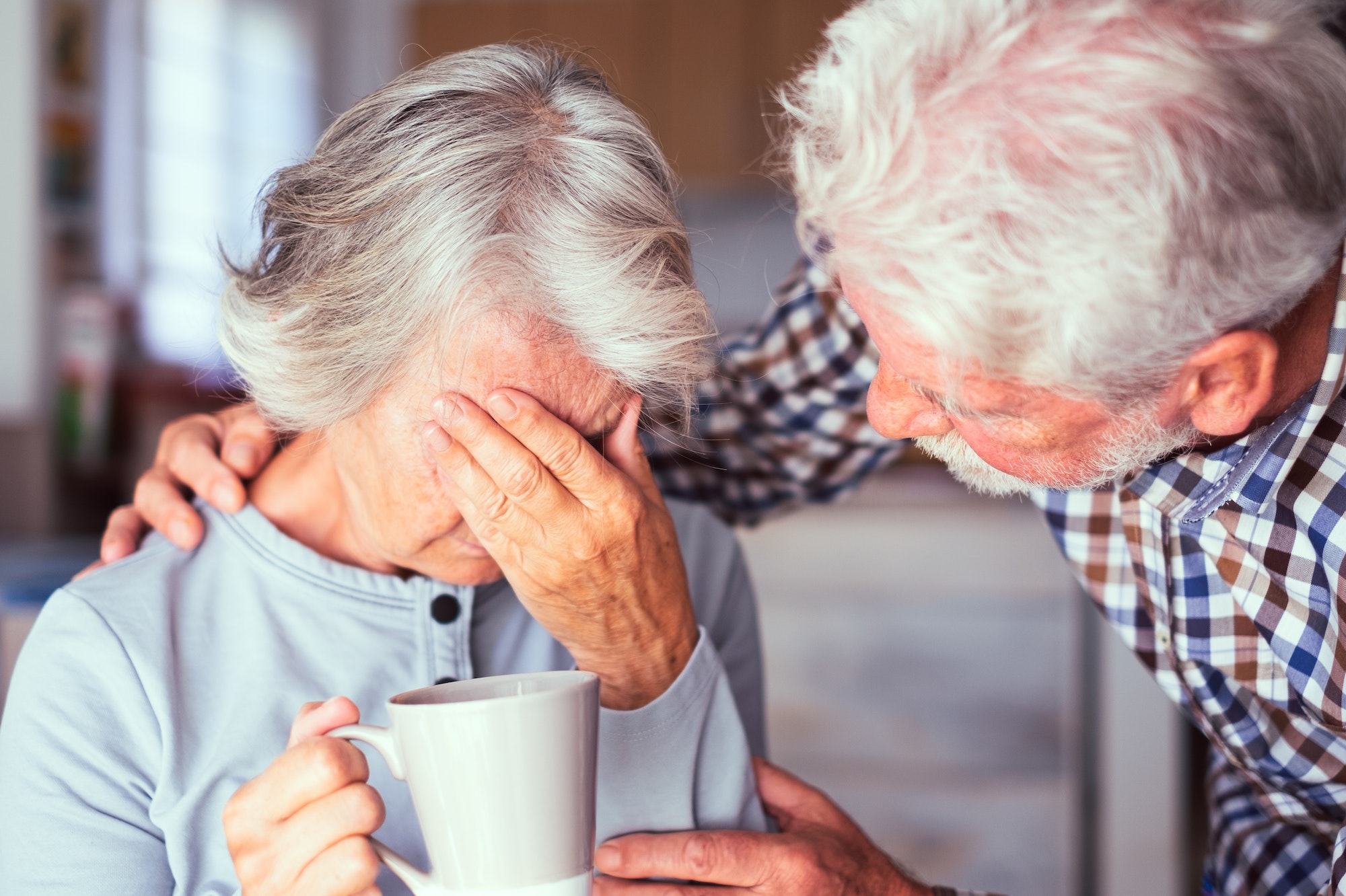 Old senior man comforting his depressed illness wife, unhappy elderly woman at home